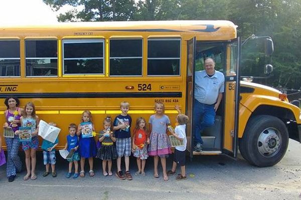 driver standing in doorway of a school bus with kids lined up along the bus wall