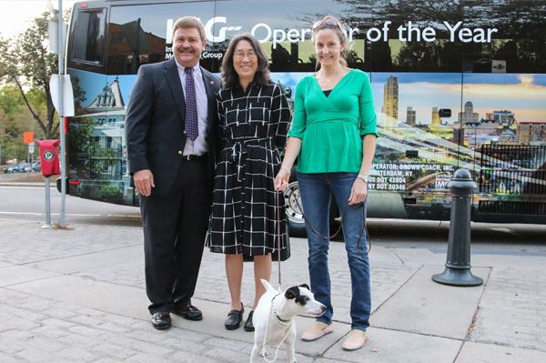 a man, two women, and a dog standing in front of a bus labeled "Operator of the Year"